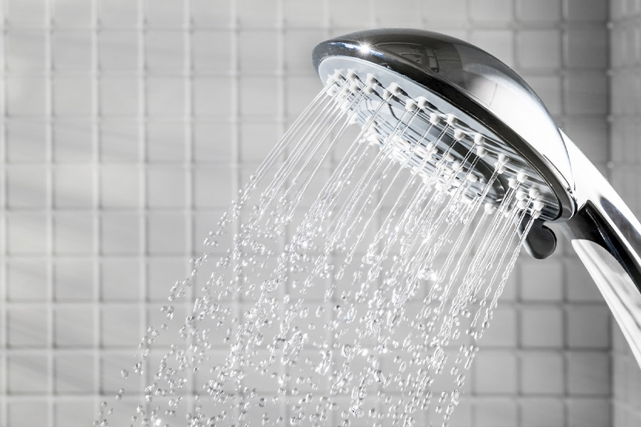 Up close shot of a chrome shower head with running water in a white tiled shower stall.